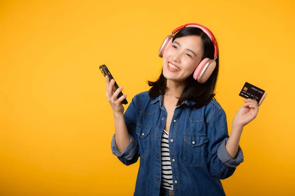デニムの服を着た笑顔とスマートフォンやクレジットカードを持つヘッドフォンを身に着けて幸せな成功を収めた肖像アジアの若い女性 ショッピングオンライン携帯電話エンターテイメントライフスタイルコンセプト — ストック写真