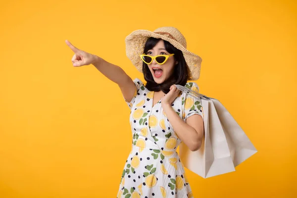 stock image Portrait attractive happy young asian woman with trendy springtime dress, hat, sunglasses fashion and paper bag isolated on yellow background. Summertime sale shopping concept.