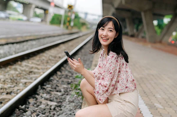バンコクの鉄道駅の横にある携帯電話を使ってバスケットを編む若いアジアの女性旅行者 旅のライフスタイル 世界旅行探検家またはアジアの夏の観光コンセプト — ストック写真