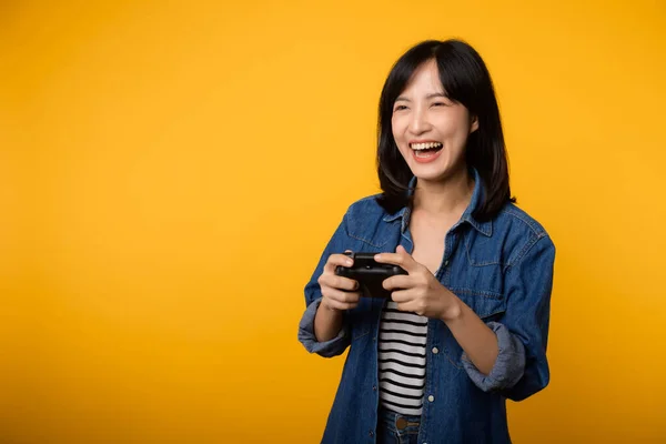 stock image Portrait asian young woman with happy success smile wearing denim clothes holding joystick controller and playing video game. Fun and relax hobby entertainment lifestyle concept.