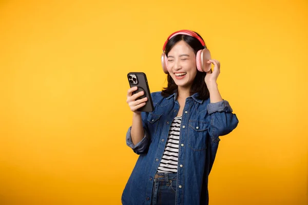ポートレート若い陽気なアジアの女性は黄色に対するスマートフォン音楽アプリケーションによる音声を聞くことをお楽しみください ヘッドフォンで幸せな笑顔の女性の人 レジャー ライフスタイル テクノロジーの概念 — ストック写真