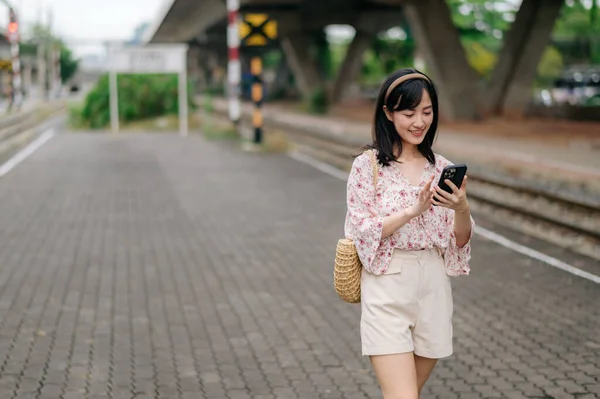 Młoda Azjatka Podróżująca Koszem Tkackim Pomocą Telefonu Komórkowego Obok Dworca — Zdjęcie stockowe