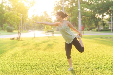 Kadın koşucu. Açık havada koşup eğlenmeden önce yeşil spor kıyafetli sağlıklı bir Asyalı genç kadın parkta kaslarını esnetiyor. Kamu parkındaki spor koşucusu kız. Refah konsept demek.