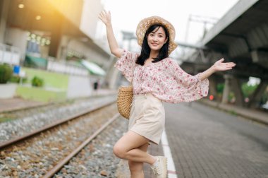 Tren yolunun yanındaki kameraya gülümseyen sepetli Asyalı genç kadın gezgin. Seyahat yaşam tarzı, dünya turisti ya da Asya yaz turizmi konsepti.