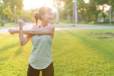 Kadın koşucu. Açık havada koşup eğlenmeden önce yeşil spor kıyafetli sağlıklı bir Asyalı genç kadın parkta kaslarını esnetiyor. Kamu parkındaki spor koşucusu kız. Refah konsept demek.