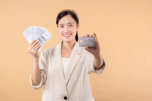 成功的快乐而自信的亚洲女商人的肖像 身穿白色夹克 手持现金美元和信用卡 站在米色背景之上 百万富翁业务 购物概念 — 图库照片