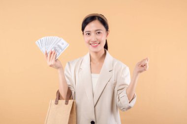 Beyaz ceketli, para dolu beyaz ceketli ve bej arka planda duran başarılı, kendine güvenen genç Asyalı iş kadınının portresi. Çevre dostu alışveriş kavramı.