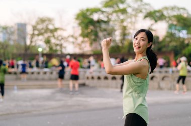 Kadın koşucu. Yeşil spor giyim aerobiği olan formda bir Asyalı genç kadın parkta dans ediyor ve açık havada eğleniyor. Kamu parkındaki spor koşucusu kız. Refah konsept demek.