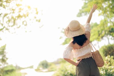 Dokuma şapkası ve sepeti ve yeşil halka açık park arka planında kamerası olan Asyalı genç bir kadın gezginin portresi. Seyahat yaşam tarzı, dünya turisti ya da Asya yaz turizmi konsepti.
