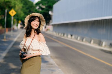 Dokuma şapkası ve sepeti ve yeşil halka açık park arka planında kamerası olan Asyalı genç bir kadın gezginin portresi. Seyahat yaşam tarzı, dünya turisti ya da Asya yaz turizmi konsepti.