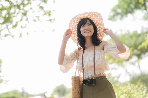 年轻的亚洲女性旅行者的肖像 戴着编织的帽子和篮子 带着绿色公园自然背景的相机 旅行生活方式 世界旅游探险家或亚洲夏季旅游概念 — 图库照片