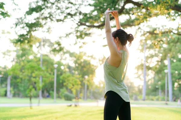 Kadın koşucu. Açık havada koşup eğlenmeden önce yeşil spor kıyafetli sağlıklı bir Asyalı genç kadın parkta kaslarını esnetiyor. Kamu parkındaki spor koşucusu kız. Refah konsept demek.