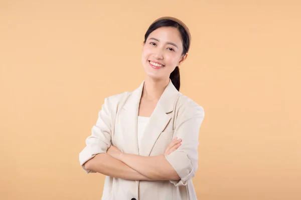 Studio portrait of successful happy confident young asian business woman. Beautiful young lady in white jacket smiling at camera standing isolated on solid beige colour copyspace background