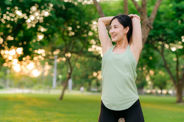 Female jogger. Fit Asian young woman with green sportswear stretching muscle in park before running and enjoying a healthy outdoor. Fitness runner girl in public park. Wellness being concept