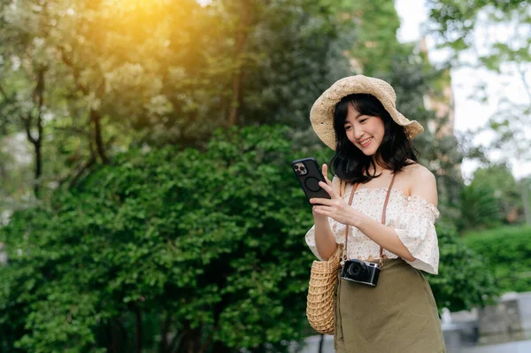 stock image Portrait of young asian woman traveler with weaving hat, basket, mobile phone and camera on green public park background. Journey trip lifestyle, world travel explorer or Asia summer tourism concept.