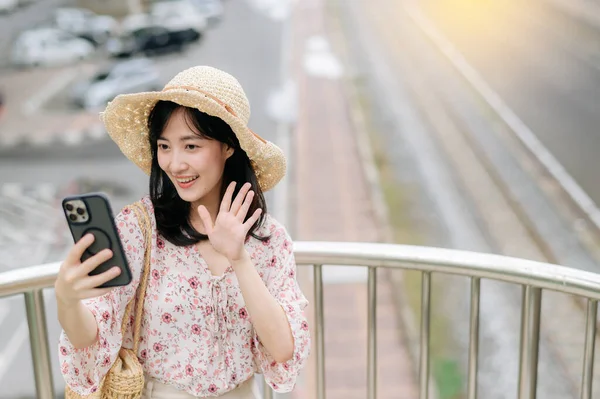 stock image asian young woman traveler with weaving basket using mobile phone and standing on overpass with railway background. Journey trip lifestyle, world travel explorer or Asia summer tourism concept.