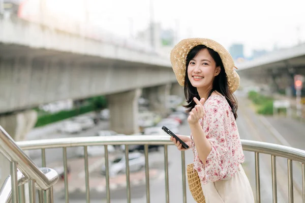 亚洲年轻女性旅行者 带着编织篮子 使用手机 站在有铁路背景的立交桥上 旅行生活方式 世界旅游探险家或亚洲夏季旅游概念 — 图库照片