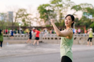 Kadın koşucu. Yeşil spor giyim aerobiği olan formda bir Asyalı genç kadın parkta dans ediyor ve açık havada eğleniyor. Kamu parkındaki spor koşucusu kız. Refah konsept demek.