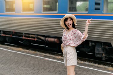 Elinde sepet olan Asyalı genç bir kadın gezgin, arkasını dönüp arkasına bile bakmadan trene gülümsüyor. Seyahat yaşam tarzı, dünya turisti ya da Asya yaz turizmi konsepti.