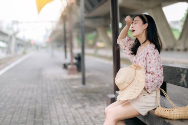 Elinde sepetle tren istasyonunda bekleyen Asyalı genç bir gezgin kadın. Seyahat yaşam tarzı, dünya turisti ya da Asya yaz turizmi konsepti.