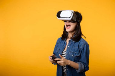 Asyalı genç bir kadın sanal gerçeklik kulaklığı takarak ve kumandayı sarı arka planda tutarak mutlu bir başarı elde etti. Sanal gelecek video oyunu konseptini kazanan.