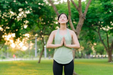 Kadın koşucu. Açık havada koşup eğlenmeden önce yeşil spor kıyafetli sağlıklı Asyalı genç bir kadın parkta temiz hava soluyor. Kamu parkındaki spor koşucusu kız. Refah konsept demek.