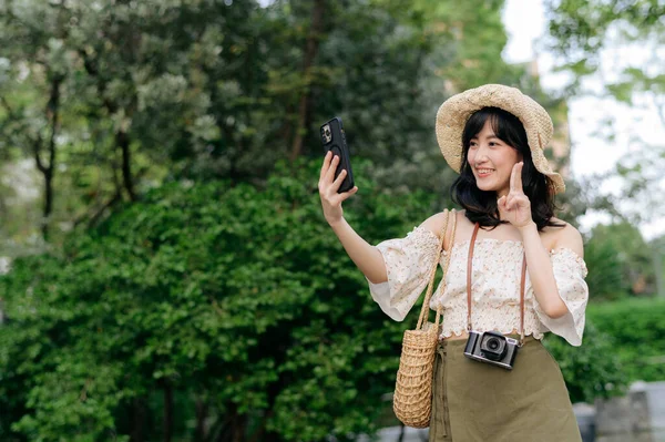 带着编织帽 手机和相机的年轻亚洲女性游客在绿色公园背景下的肖像 旅行生活方式 世界旅游探险家或亚洲夏季旅游概念 — 图库照片