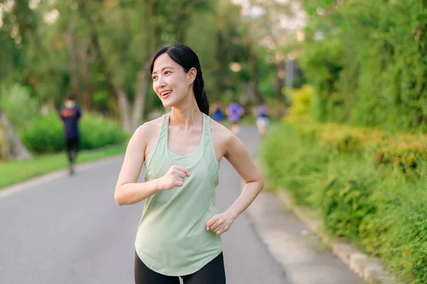 适合年轻的亚洲女子在公园里慢跑 面带微笑快乐地跑步 享受健康的户外生活 女慢跑者 健身跑步的女孩在公共公园 健康的生活方式和幸福的概念 — 图库照片