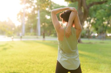 Kadın koşucu. Açık havada koşup eğlenmeden önce yeşil spor kıyafetli sağlıklı bir Asyalı genç kadın parkta kaslarını esnetiyor. Kamu parkındaki spor koşucusu kız. Refah konsept demek.