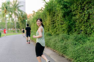 Genç, zinde Asyalı bir kadın parkta koşuyor mutlu bir şekilde koşuyor ve sağlıklı bir açık hava yaşam tarzının tadını çıkarıyor. Kadın koşucu. Kamu parkındaki spor koşucusu kız. Sağlıklı yaşam tarzı ve refah kavramı