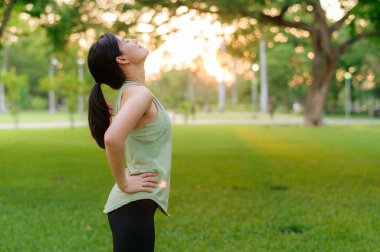 Kadın koşucu. Açık havada koşup eğlenmeden önce yeşil spor kıyafetli sağlıklı Asyalı genç bir kadın parkta temiz hava soluyor. Kamu parkındaki spor koşucusu kız. Refah konsept demek.