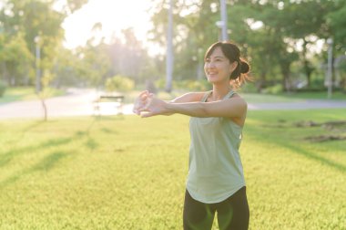 Kadın koşucu. Açık havada koşup eğlenmeden önce yeşil spor kıyafetli sağlıklı bir Asyalı genç kadın parkta kaslarını esnetiyor. Kamu parkındaki spor koşucusu kız. Refah konsept demek.