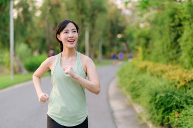 Genç, zinde Asyalı bir kadın parkta koşuyor mutlu bir şekilde koşuyor ve sağlıklı bir açık hava yaşam tarzının tadını çıkarıyor. Kadın koşucu. Kamu parkındaki spor koşucusu kız. Sağlıklı yaşam tarzı ve refah kavramı
