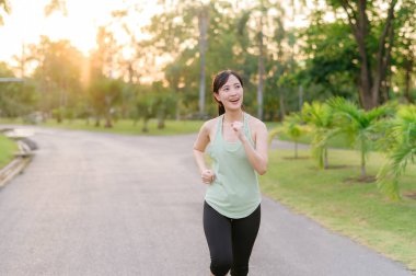 Genç, zinde Asyalı bir kadın parkta koşuyor mutlu bir şekilde koşuyor ve sağlıklı bir açık hava yaşam tarzının tadını çıkarıyor. Kadın koşucu. Kamu parkındaki spor koşucusu kız. Sağlıklı yaşam tarzı ve refah kavramı