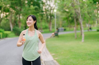 Kadın koşucu. Yeşil spor kıyafetli, sağlıklı bir açık havada koşup eğlendikten sonra organik portakal suyu içen formda bir Asyalı genç kadın. Kamu parkındaki spor koşucusu kız. Refah konsept demek.