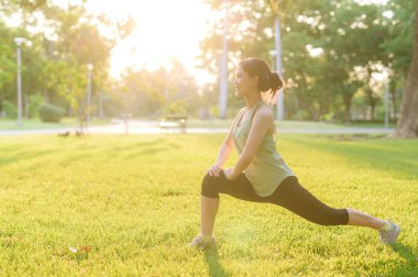 Kadın koşucu. Açık havada koşup eğlenmeden önce yeşil spor kıyafetli sağlıklı bir Asyalı genç kadın parkta kaslarını esnetiyor. Kamu parkındaki spor koşucusu kız. Refah konsept demek.