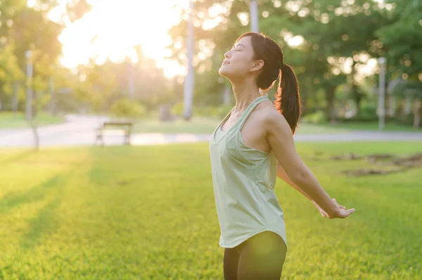 Female jogger. Fit Asian young woman with green sportswear breathing fresh air in park before running and enjoying a healthy outdoor. Fitness runner girl in public park. Wellness being concept