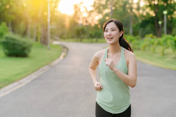 Fit young Asian woman jogging in park smiling happy running and enjoying a healthy outdoor lifestyle. Female jogger. Fitness runner girl in public park. healthy lifestyle and wellness being concept