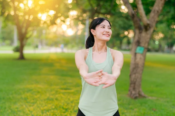 Female jogger. Fit Asian young woman with green sportswear stretching muscle in park before running and enjoying a healthy outdoor. Fitness runner girl in public park. Wellness being concept