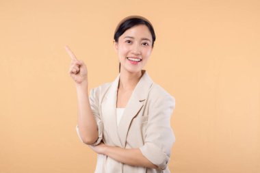 Başarılı, kendinden emin Asyalı genç iş kadınının stüdyo portresi. Beyaz ceketli güzel bir bayan kameraya gülümsüyor. Katı bej renkli arka planda tek başına duruyor.