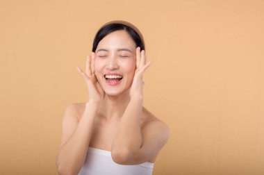 Güzel Asyalı manken bej arka planda taze, parlak, hidratlı cilde dokunuyor. Güzel yüzlü, doğal makyajlı ve sağlıklı cilt portresi olan genç bir kadın. Cilt bakımı kavramı