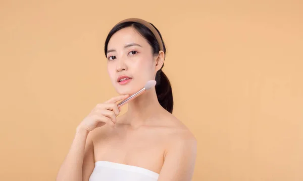 自然なメイクの顔を持つ肖像若い幸せなアジアの女性はベージュの背景に隔離化粧品の皮膚パウダーブラッシャーを保持しています 女性はスキンケアブラシ治療を適用します 美容製品化粧品のコンセプト — ストック写真