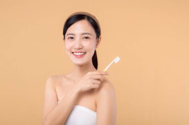 Sağlıklı gülümseyen genç bir kadının portresi. Elinde diş fırçası tutuyordu. Bej renkli stüdyo arka planında izole edilmişti. Diş temizliği, diş bakımı, diş bakımı..