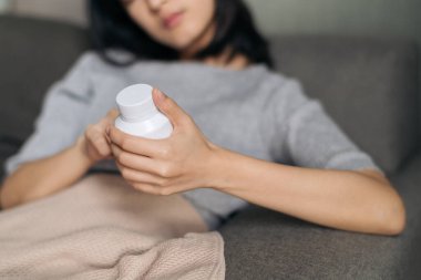 Asian woman with cold and flu reading instructions on a medicine bottle