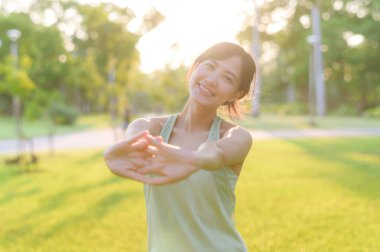 Kadın koşucu. Açık havada koşup eğlenmeden önce yeşil spor kıyafetli sağlıklı bir Asyalı genç kadın parkta kaslarını esnetiyor. Kamu parkındaki spor koşucusu kız. Refah konsept demek.