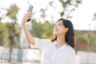Portrait beautiful young asian woman with smart mobile phone around outdoor nature view in sunny summer day