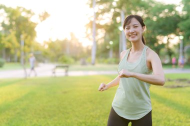 Kadın koşucu. Açık havada koşup eğlenmeden önce yeşil spor kıyafetli sağlıklı bir Asyalı genç kadın parkta kaslarını esnetiyor. Kamu parkındaki spor koşucusu kız. Refah konsept demek.