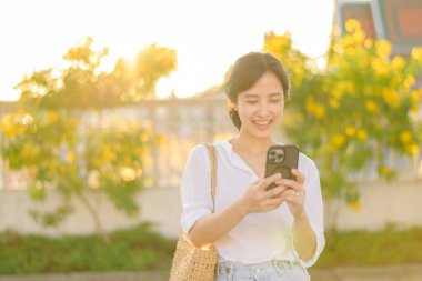 Portrait beautiful young asian woman with smart mobile phone around outdoor street view in a summer day