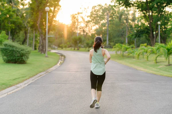 Fit young Asian woman jogging in park smiling happy running and enjoying a healthy outdoor lifestyle. Female jogger. Fitness runner girl in public park. healthy lifestyle and wellness being concept