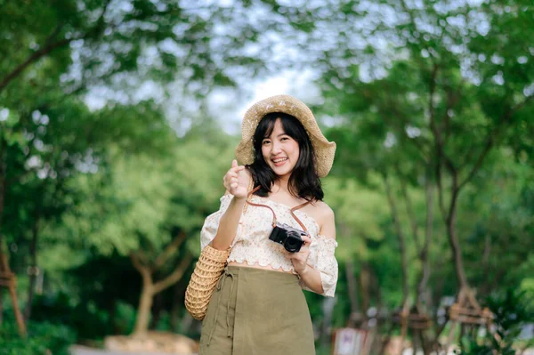 年轻的亚洲女性旅行者的肖像 戴着编织的帽子和篮子 带着绿色公园自然背景的相机 旅行生活方式 世界旅游探险家或亚洲夏季旅游概念 — 图库照片